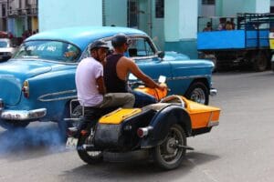 Motorcycle with sidecar riding through Cuban streets next to a blue car