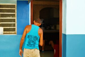 Man at the door of his house wearing a blue shirt same color than his house